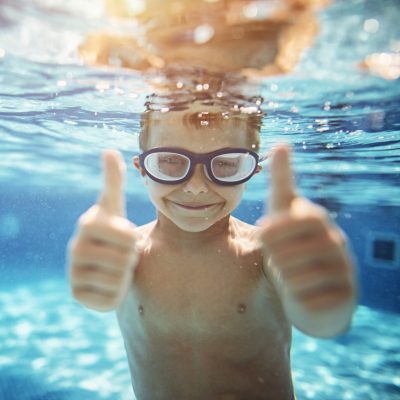 square photo of boy underwater giving thumbs up